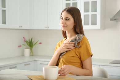 Photo of Woman holding bearded lizard in kitchen. Exotic pet