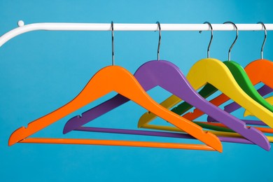 Photo of Bright clothes hangers on metal rail against light blue background, closeup