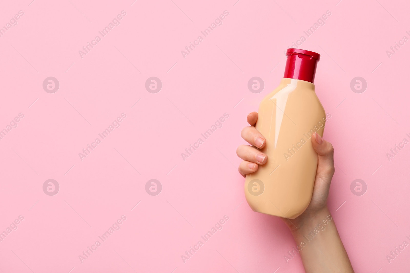 Photo of Woman holding shampoo bottle on pink background, top view. Space for text