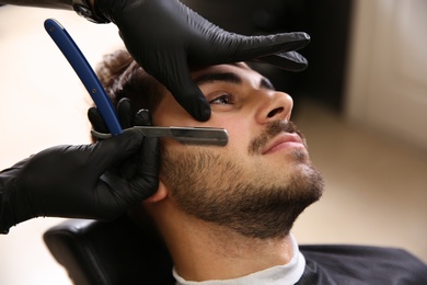 Professional hairdresser shaving client with straight razor in barbershop