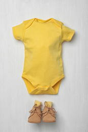 Photo of Child's bodysuit and booties on white wooden background, flat lay