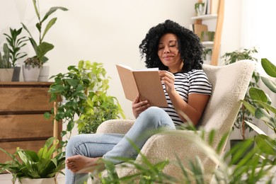 Photo of Relaxing atmosphere. Woman enjoying reading book near houseplants at home