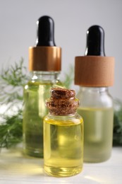 Photo of Bottles of essential oil and fresh dill on light table, closeup