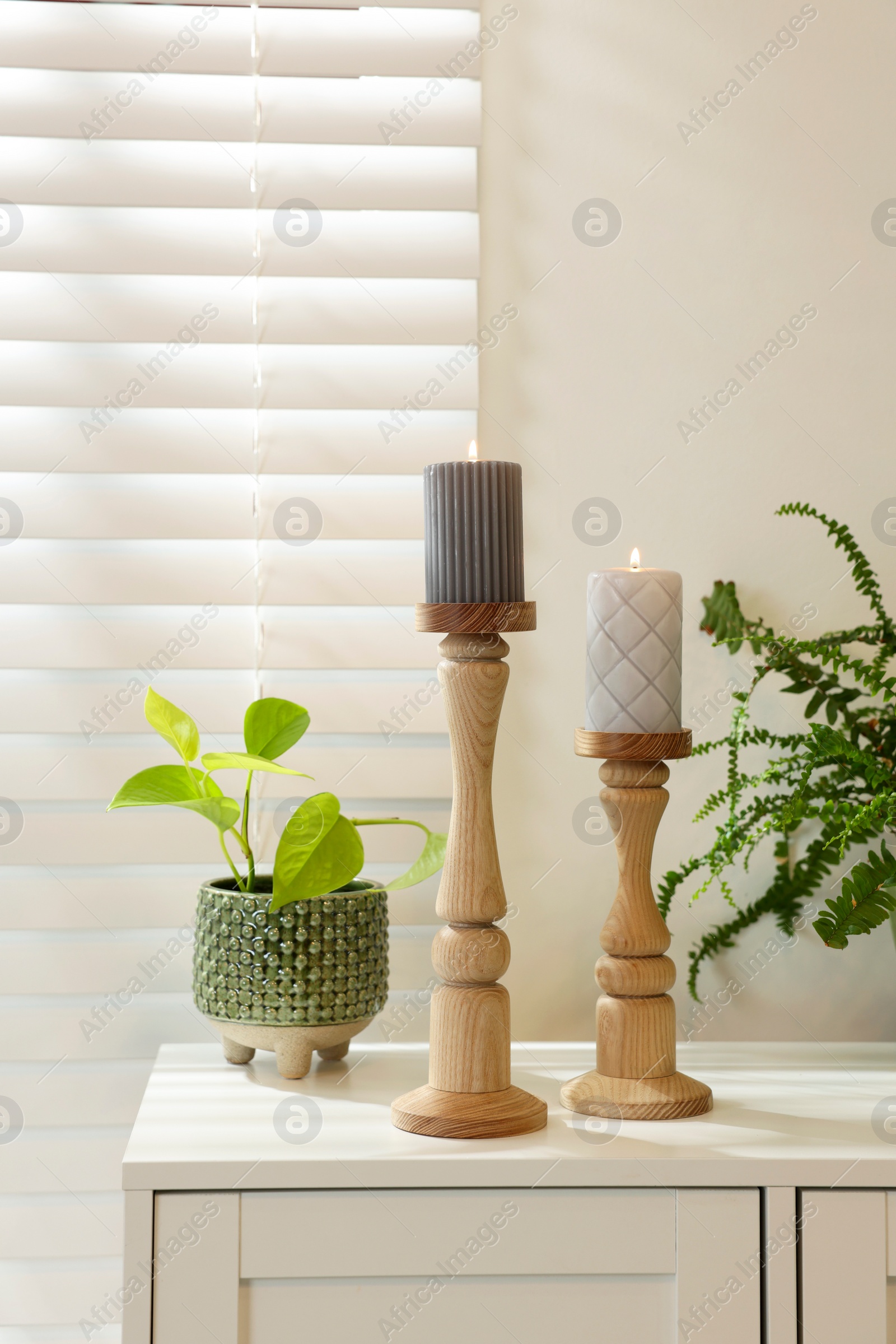 Photo of Pair of beautiful wooden candlesticks and houseplants on white table in room