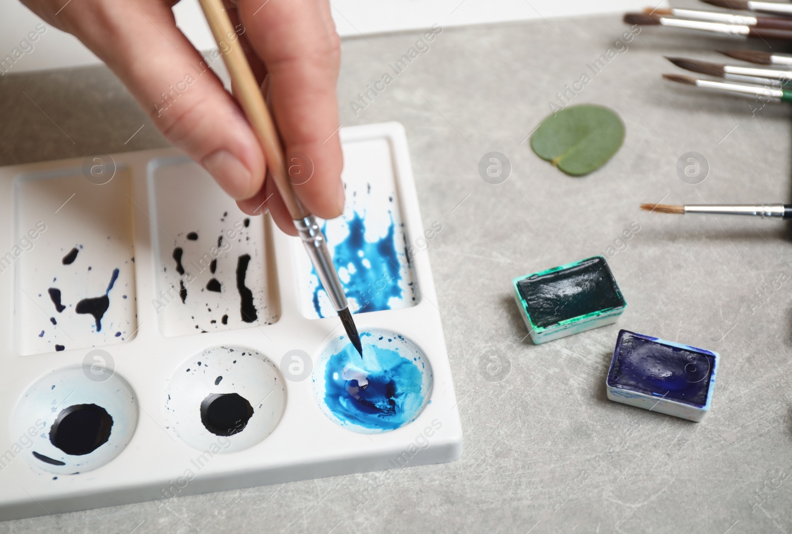 Photo of Woman painting with watercolor at grey stone table, closeup