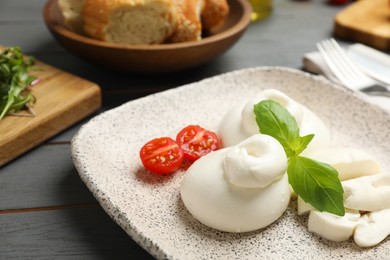 Photo of Delicious burrata cheese with basil and cut tomato on grey wooden table, closeup