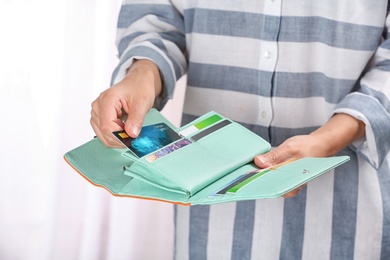 Photo of Woman taking out credit card from stylish wallet on light background, closeup