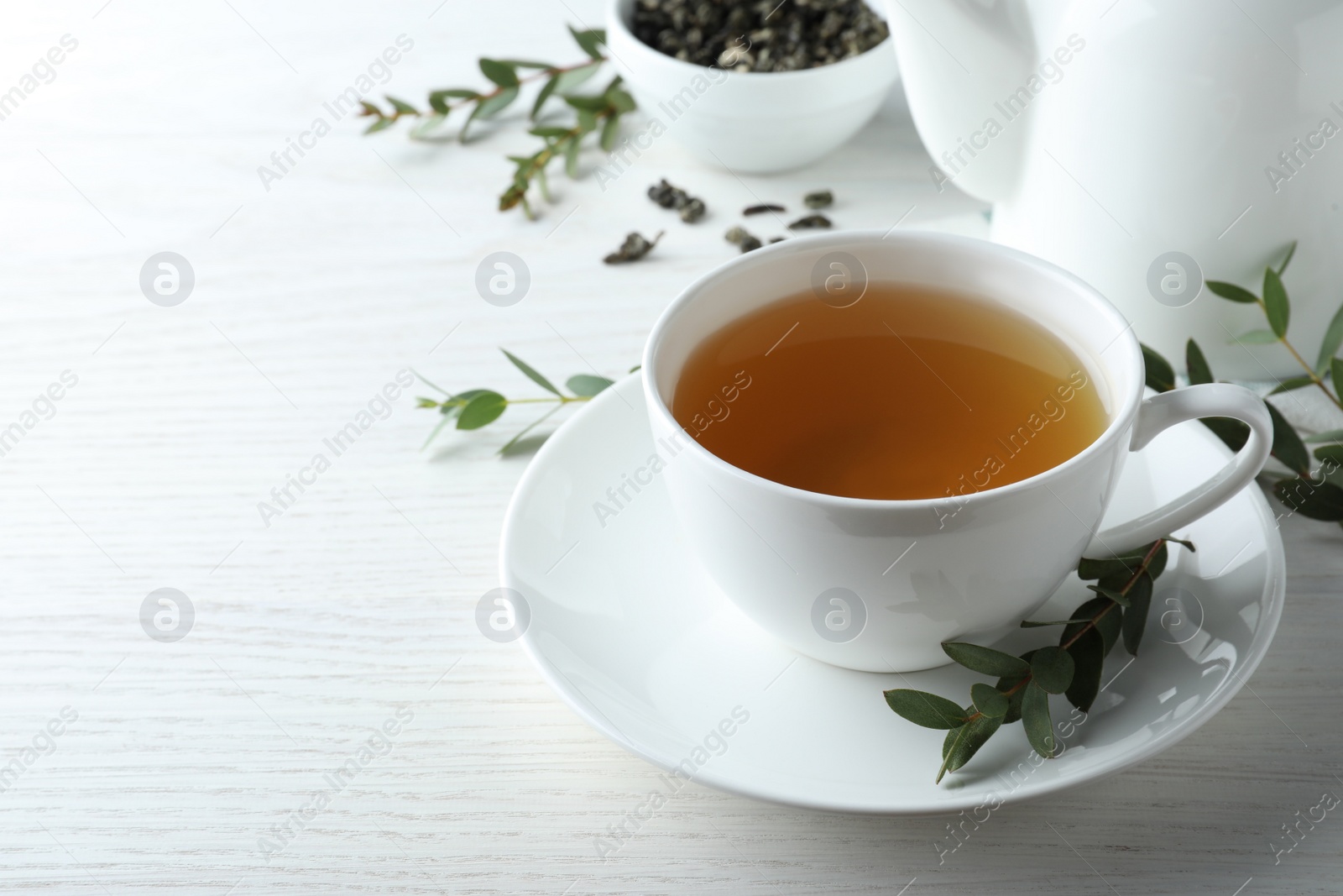 Photo of Cup of green tea and eucalyptus leaves on white wooden table. Space for text