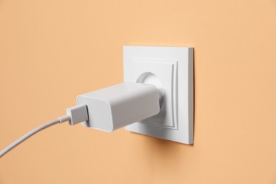 Photo of Charger adapter plugged into power socket on pale orange wall, closeup. Electrical supply