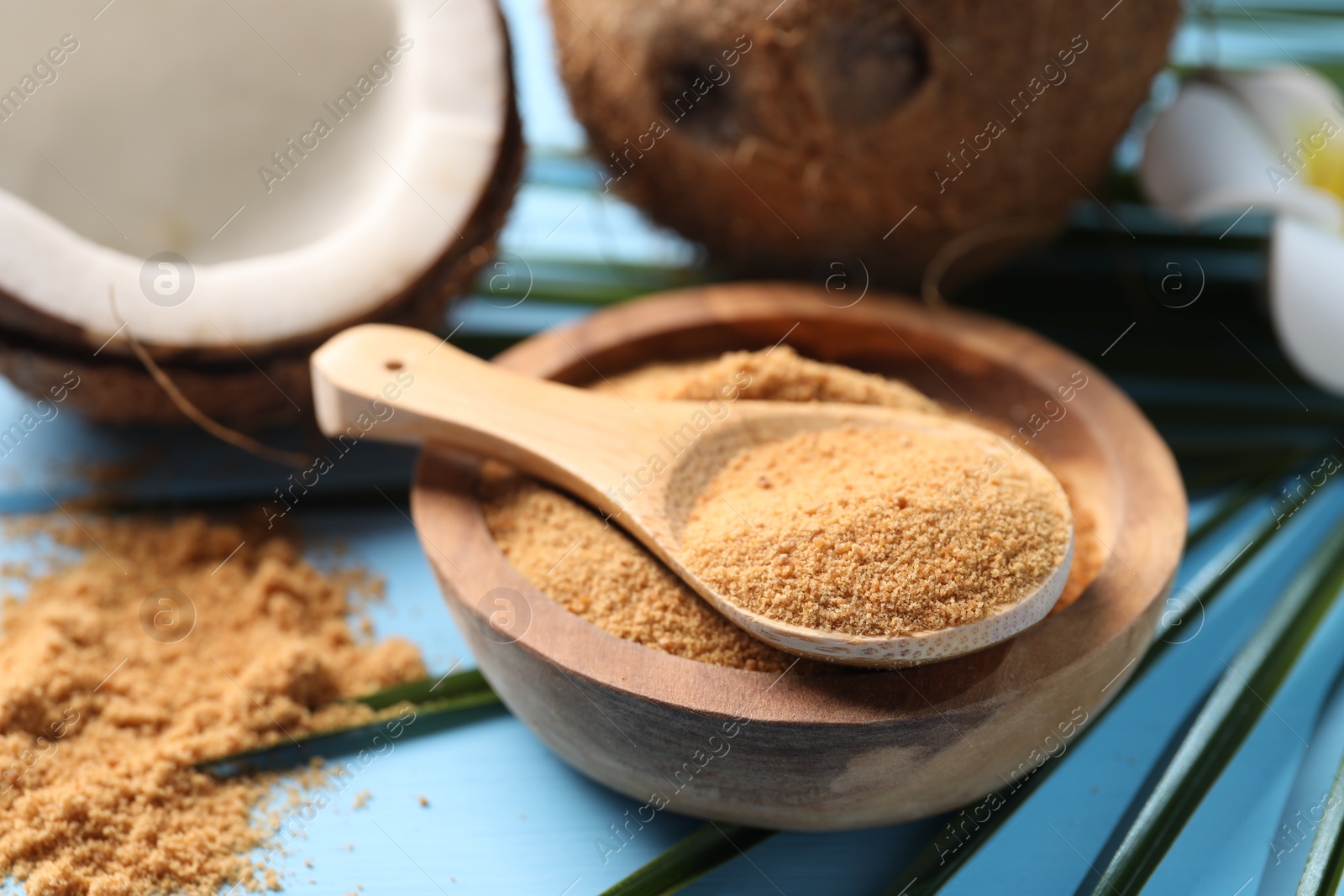 Photo of Coconut sugar in bowl, spoon and fruits on light blue wooden table, closeup