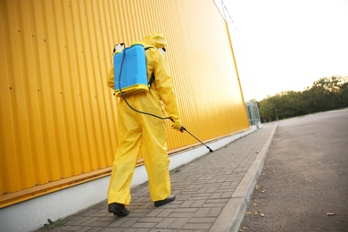 Photo of Person in hazmat suit disinfecting street with sprayer, back view. Surface treatment during coronavirus pandemic