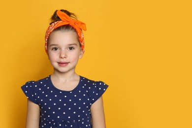 Photo of Cute little girl wearing stylish bandana on orange background, space for text