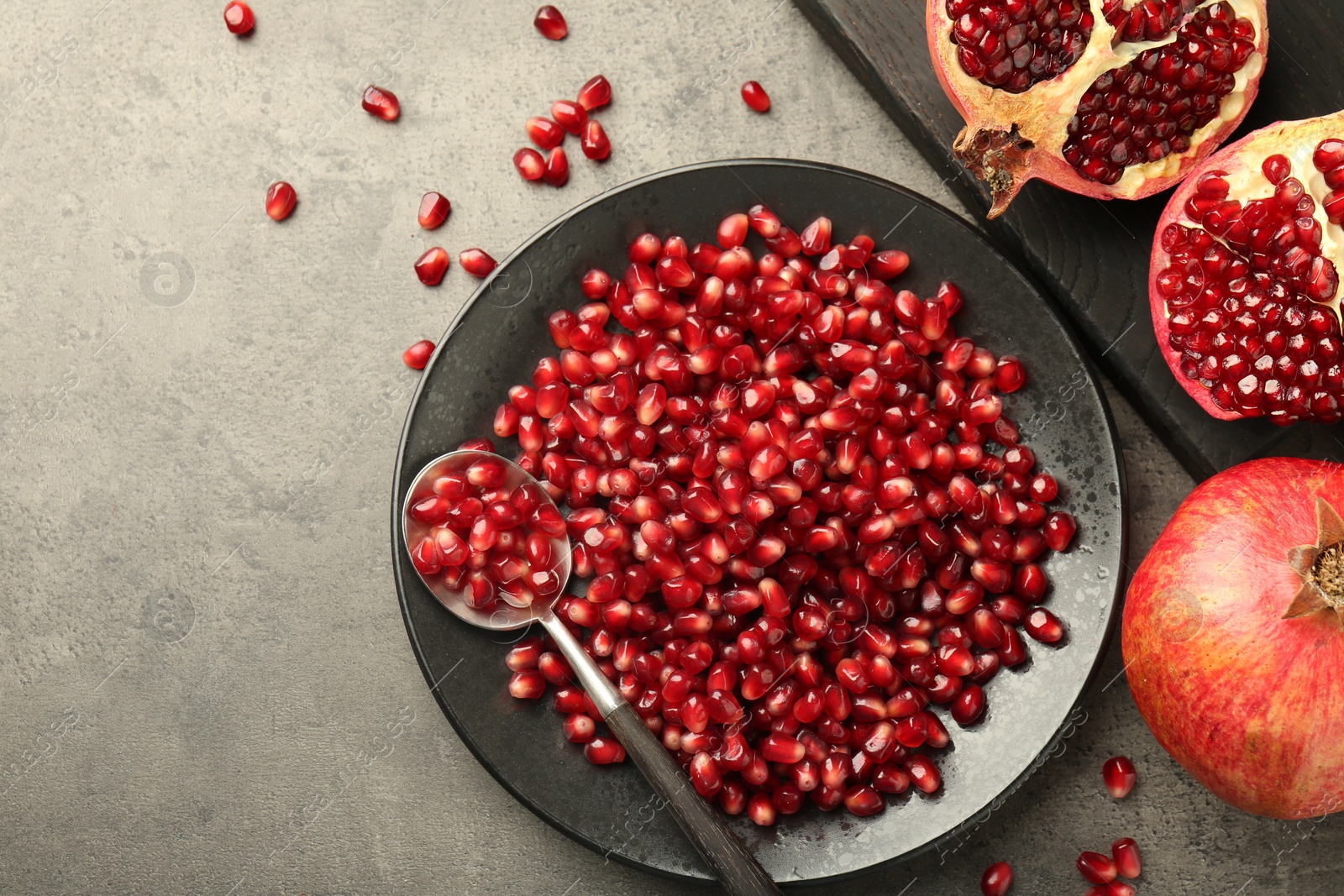 Photo of Ripe juicy pomegranate grains on grey textured table, flat lay. Space for text