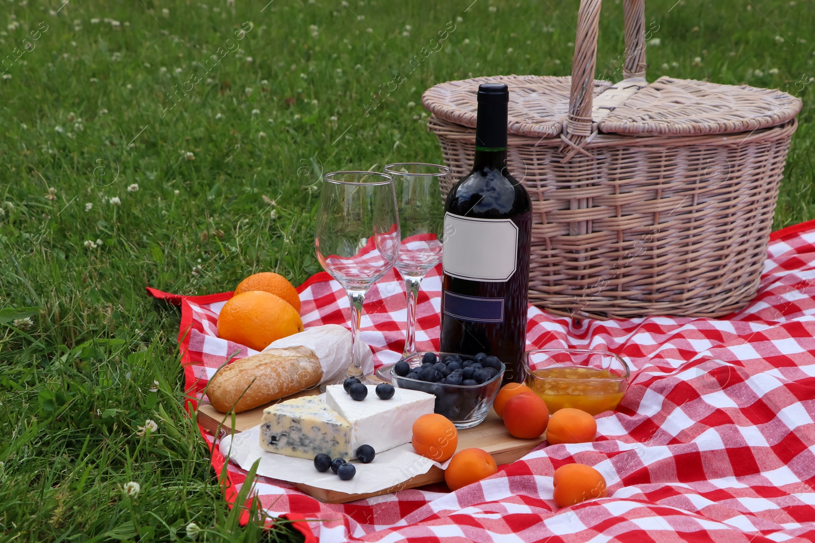 Photo of Picnic blanket with delicious food and wine outdoors on summer day