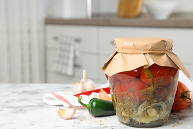 Pickled tomatoes in glass jar and products on white marble table in kitchen