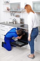 Housewife with repairman near modern oven in kitchen