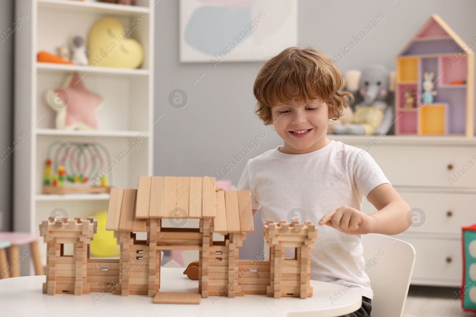 Photo of Little boy playing with wooden entry gate at white table in room. Child's toy