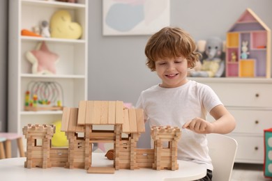 Photo of Little boy playing with wooden entry gate at white table in room. Child's toy