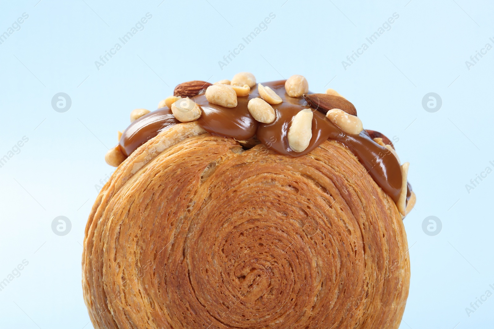 Photo of One supreme croissant with chocolate paste and nuts on light blue background, closeup. Tasty puff pastry