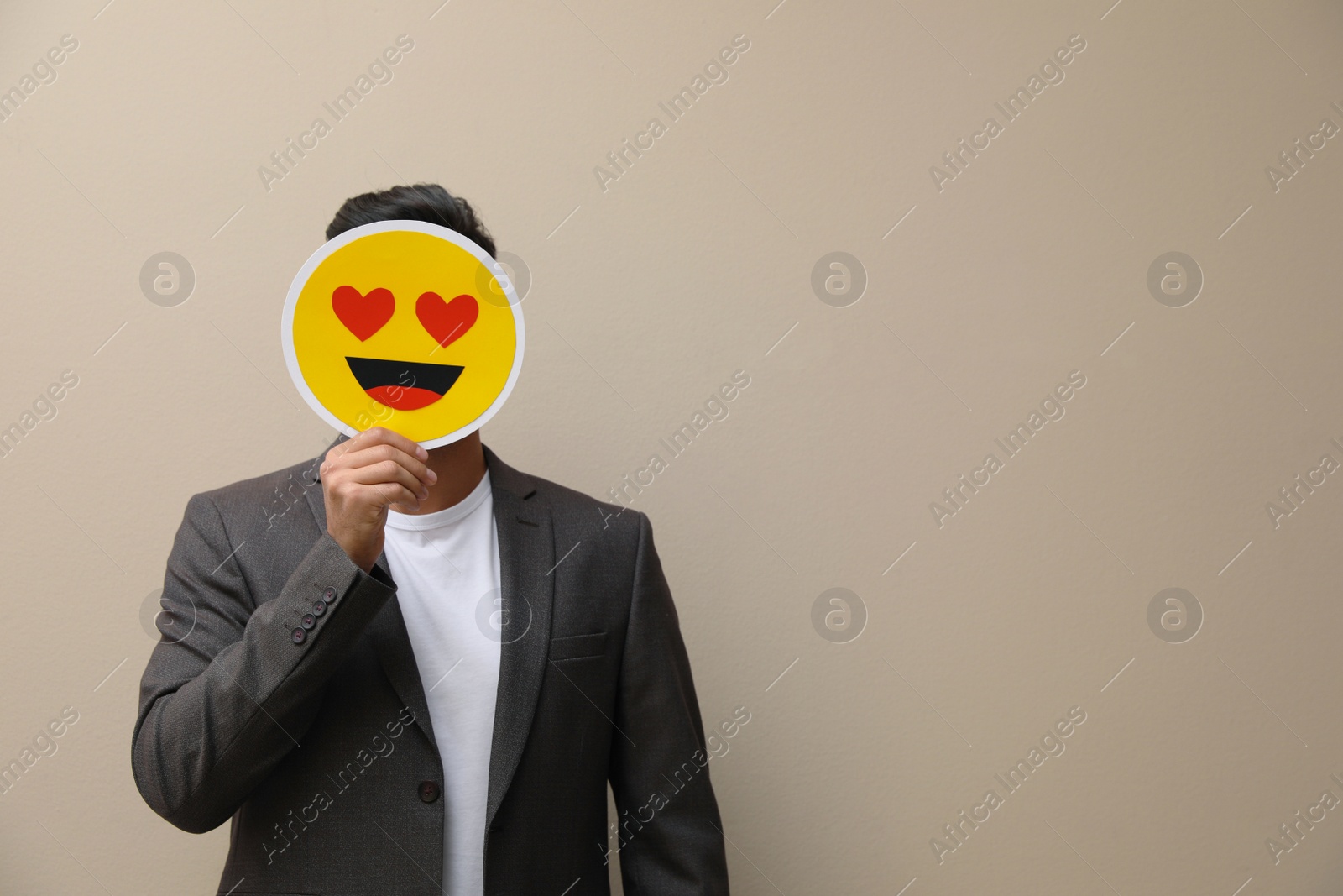 Photo of Man hiding emotions using card with drawn smiling face on beige background. Space for text