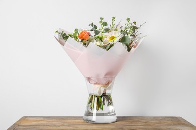 Bouquet of beautiful flowers in vase on wooden table against white wall