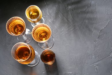 Photo of Many different liqueurs in glasses on dark textured table, flat lay. Space for text