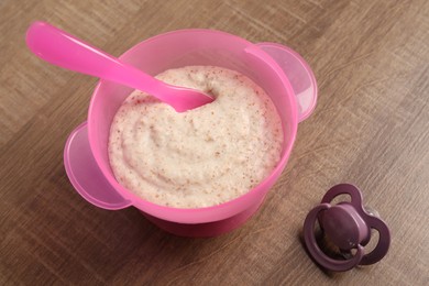Photo of Baby food. Puree in bowl and soother on wooden table