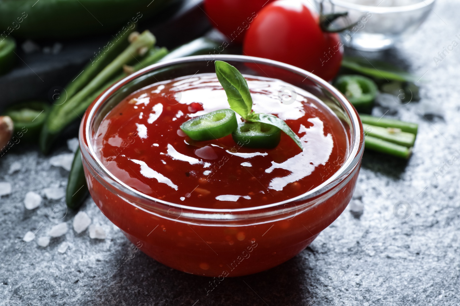 Photo of Spicy chili sauce in glass bowl on grey table, closeup