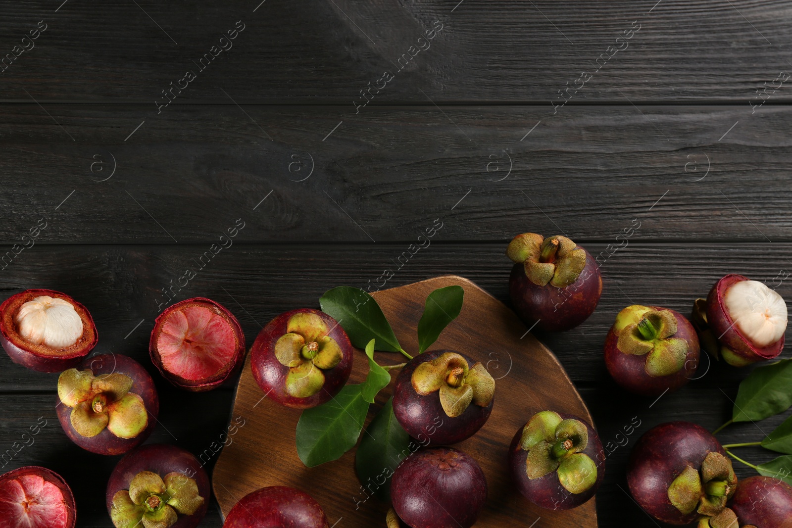 Photo of Fresh ripe mangosteen fruits on dark wooden table, flat lay. Space for text