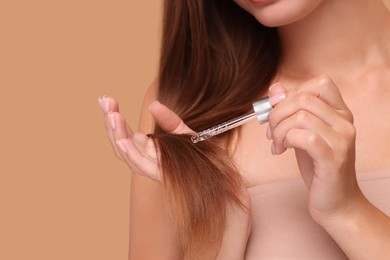 Woman applying serum onto hair on beige background, closeup