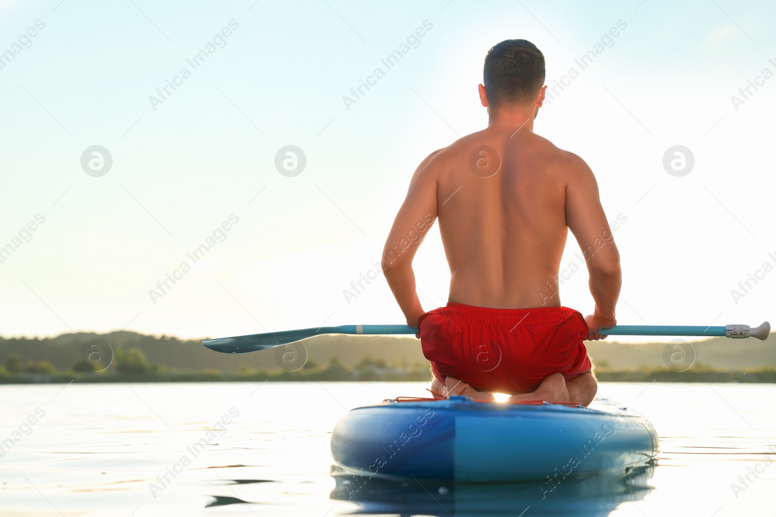 Photo of Man paddle boarding on SUP board in river at sunset, back view