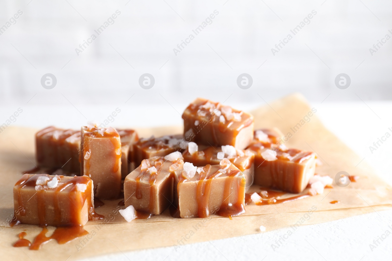 Photo of Tasty candies, caramel sauce and salt on white table, closeup