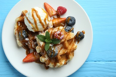 Photo of Delicious Belgian waffles with ice cream, berries and caramel sauce on light blue wooden table, top view