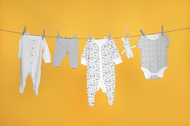 Baby clothes and bunny toy drying on laundry line against orange background