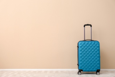 Photo of Modern suitcase on floor near light wall. Space for text