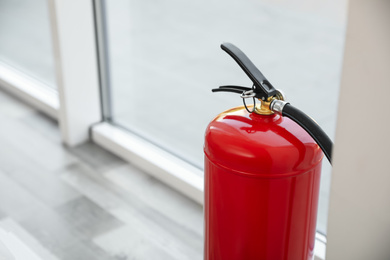 Photo of Fire extinguisher near window indoors, closeup. Space for text
