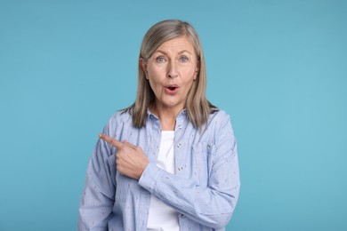 Photo of Surprised senior woman pointing at something on light blue background