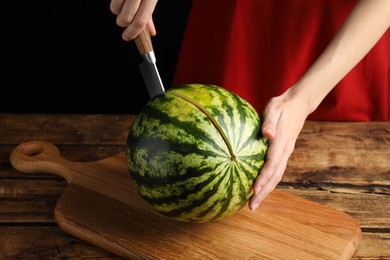 Photo of Woman cutting delicious watermelon at wooden table against black background, closeup