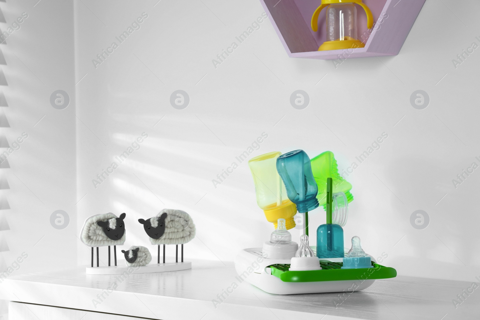 Photo of Dryer with baby bottles and nipples after sterilization near decor on white table