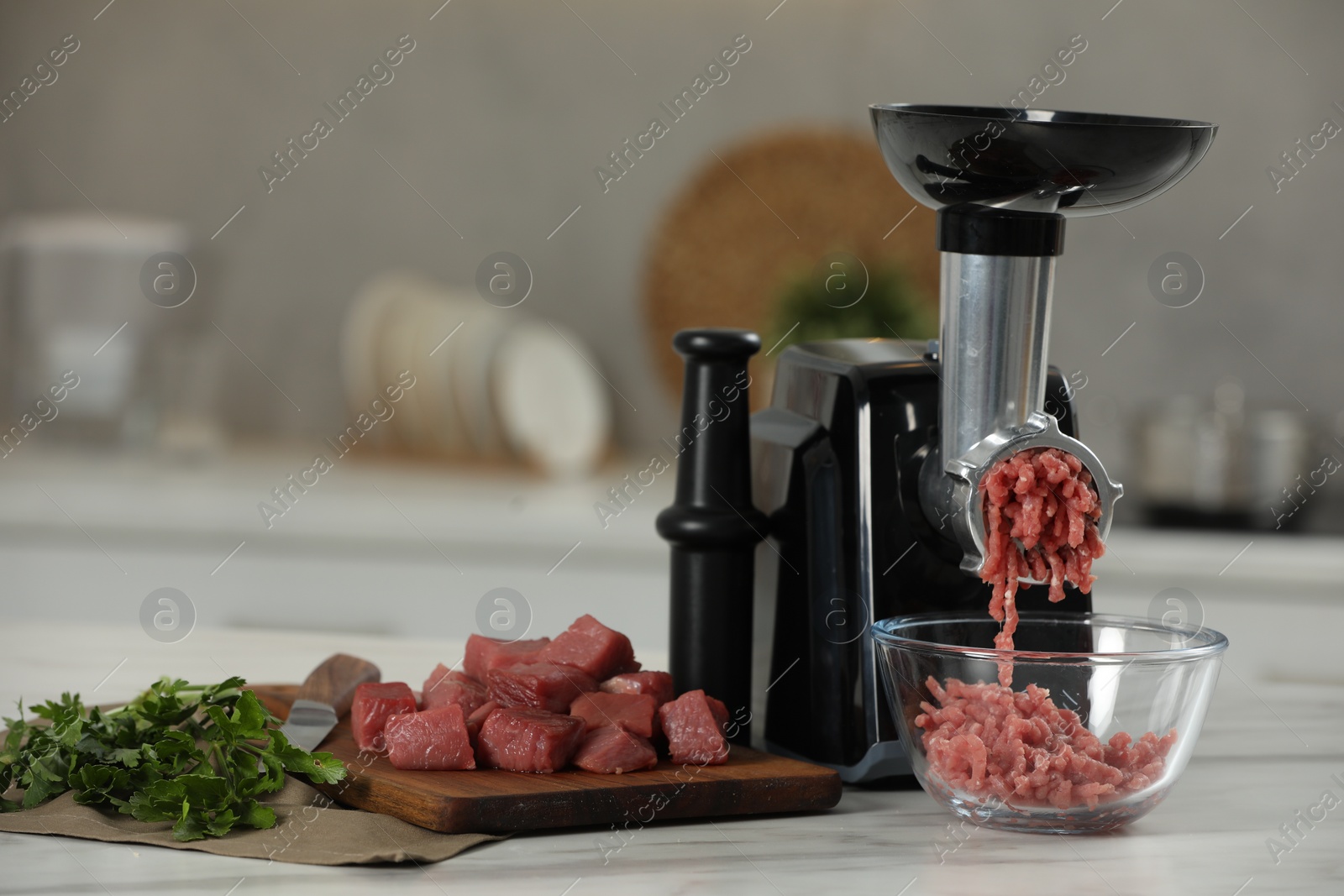 Photo of Electric meat grinder with beef mince and parsley on white table in kitchen, closeup