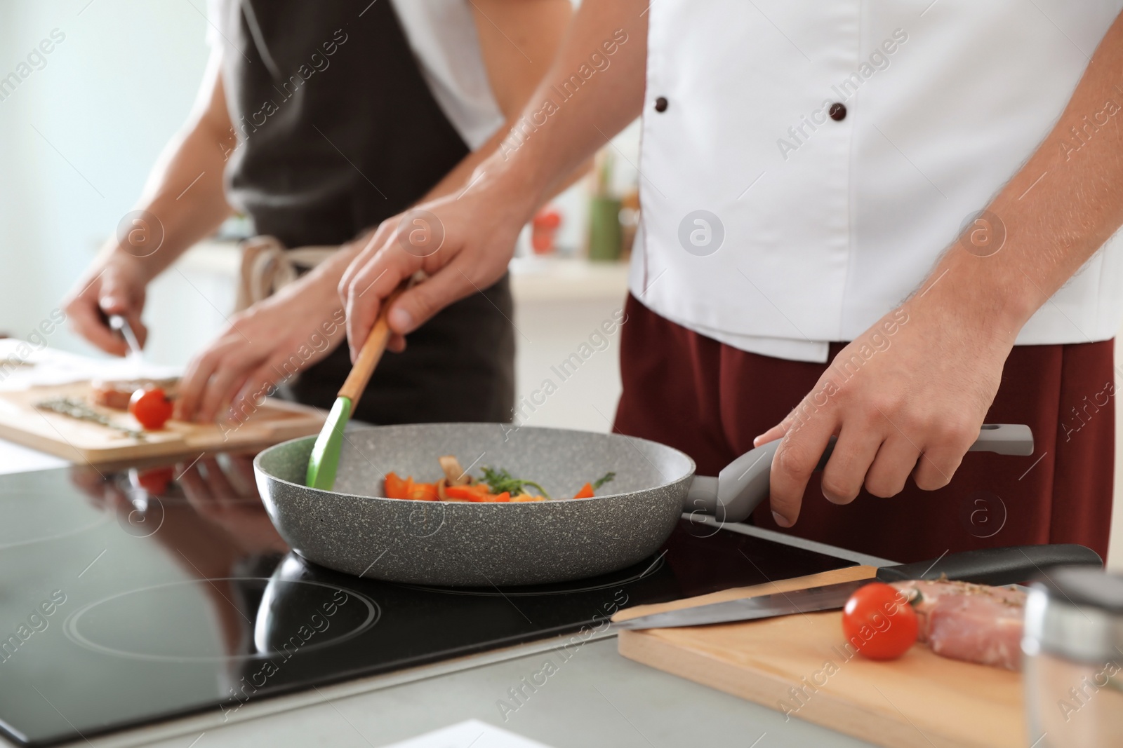 Photo of Male chef cooking vegetables on electric stove, closeup