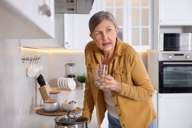 Photo of Menopause. Woman with glass of water suffering from hot flash in kitchen