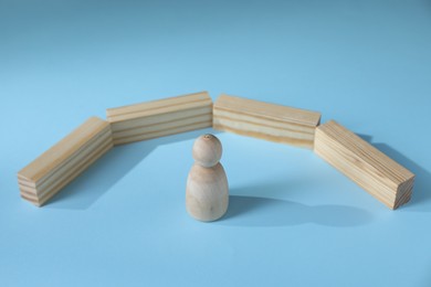 Photo of Overcoming barries for development and success. Wooden human figure movement blocked by blocks on light blue background, closeup