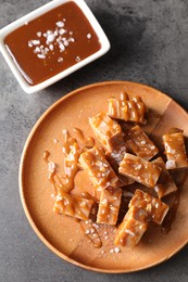 Plate with tasty candies, caramel sauce and salt on grey table, top view