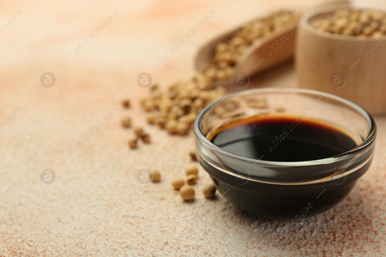 Photo of Soy sauce in bowl and beans on beige textured table, closeup. Space for text