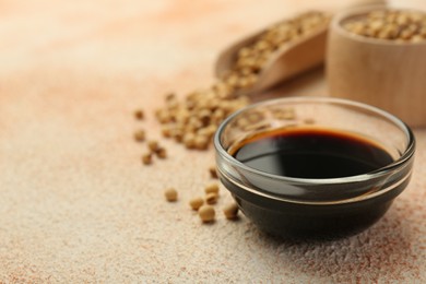 Soy sauce in bowl and beans on beige textured table, closeup. Space for text