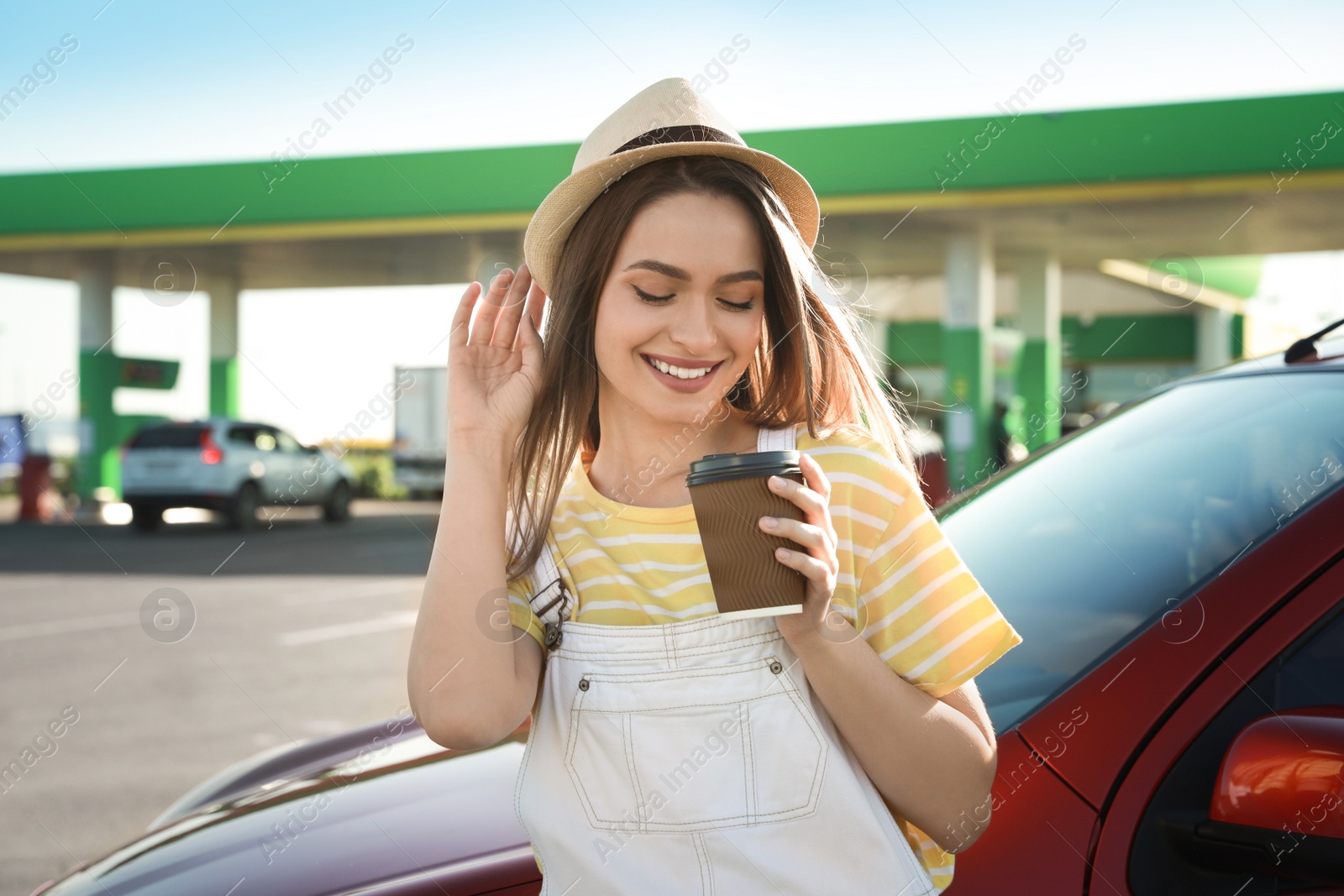 Photo of Beautiful young woman with coffee near car at gas station