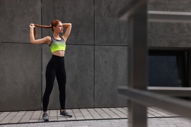Beautiful woman in stylish gym clothes posing near grey wall on street