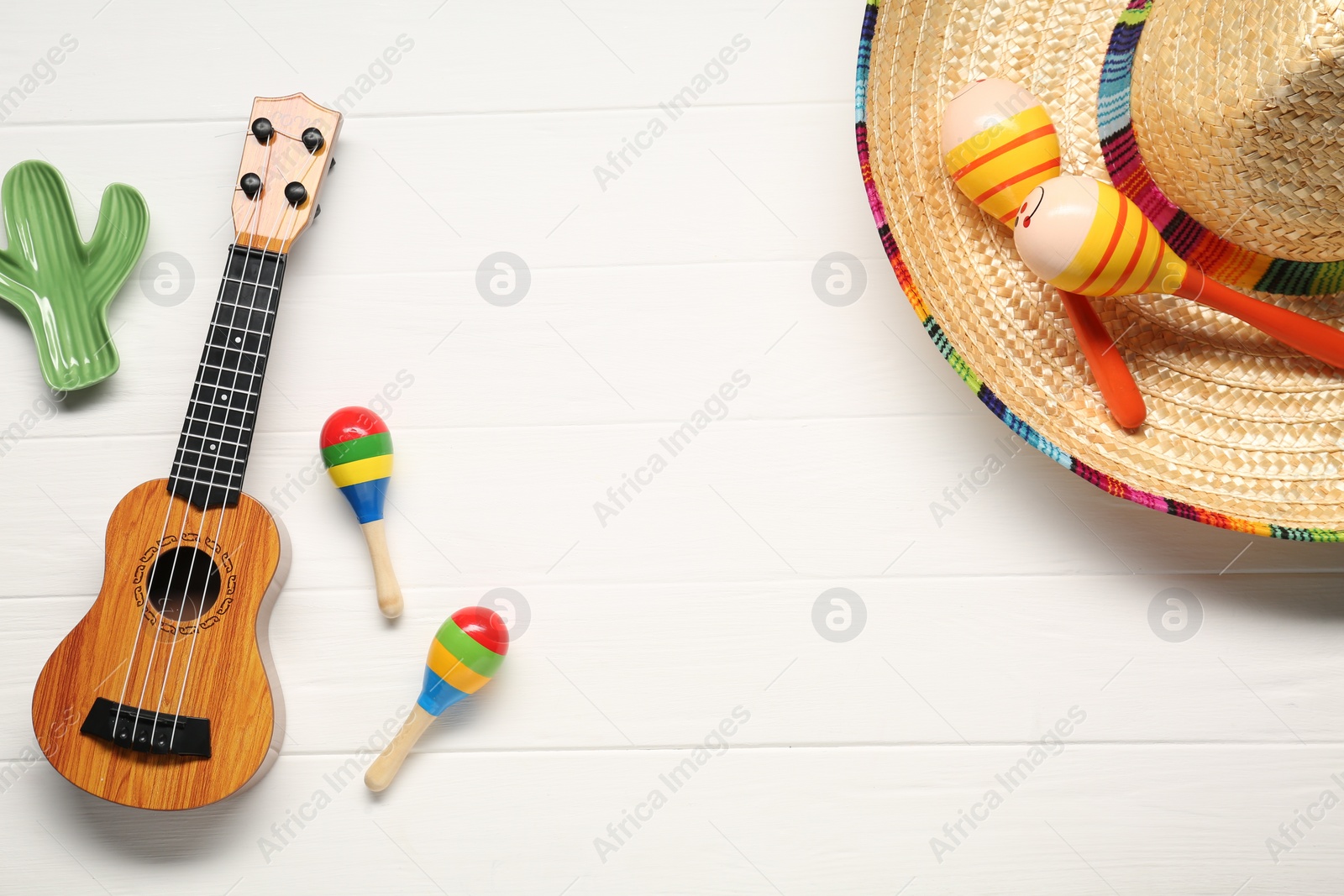 Photo of Mexican sombrero hat, maracas, toy cactus and guitar on white wooden background, flat lay. Space for text