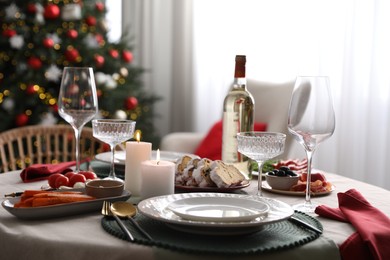 Photo of Christmas table setting with burning candles, appetizers and dishware indoors